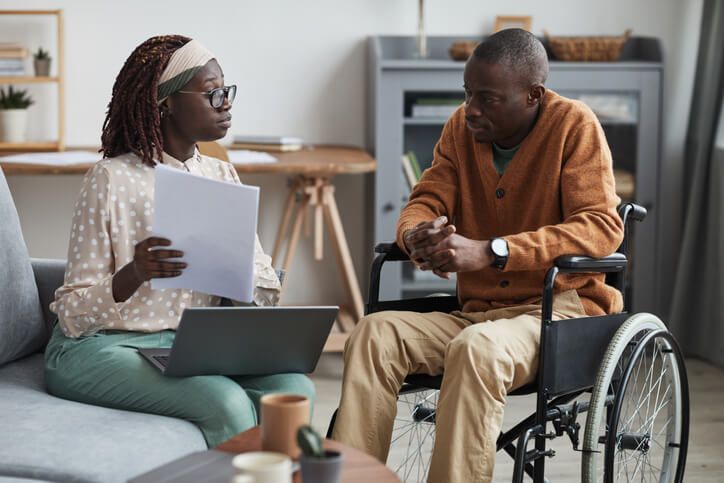 A social service worker training graduate speaking with an elderly client in a wheelchair