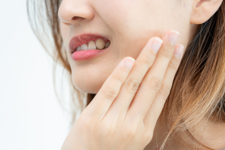 A female patient holding her face indicating possible oral disease to a dental assistant after her dental assistant training