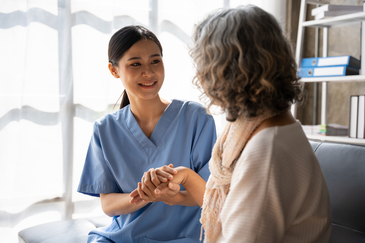 A female healthcare assistant interacting with a smiling elderly patient after completing her healthcare assistant training