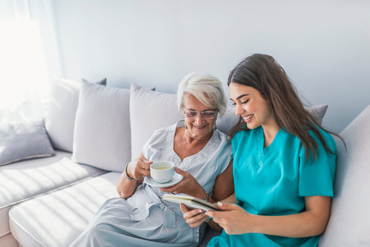 A healthcare assistant training grad sitting with an elderly client with a cup of tea
